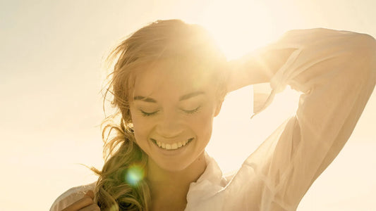 Une femme souriante grâce à la vitamine D et au soleil qui brille sur elle